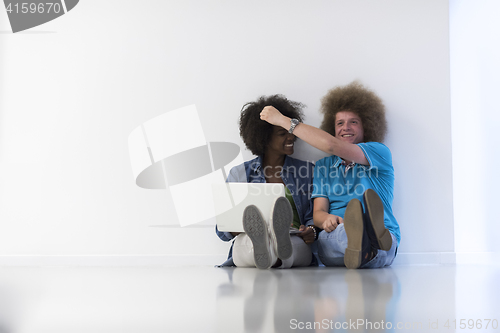 Image of multiethnic couple sitting on the floor with a laptop and tablet
