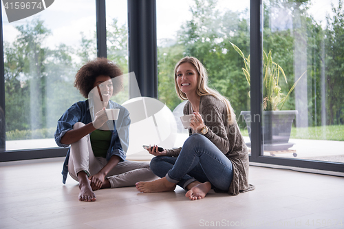 Image of multiethnic women sit on the floor and drinking coffee