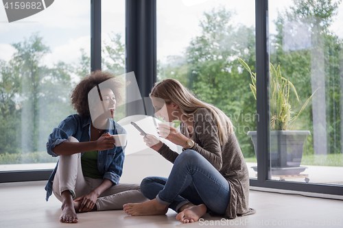 Image of multiethnic women sit on the floor and drinking coffee