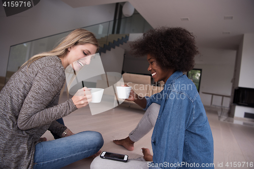 Image of young multiethnic women sit on the floor and drinking coffee