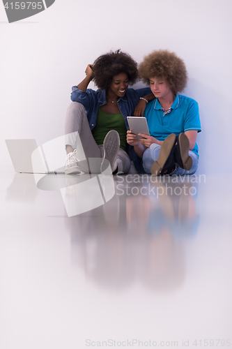 Image of multiethnic couple sitting on the floor with a laptop and tablet