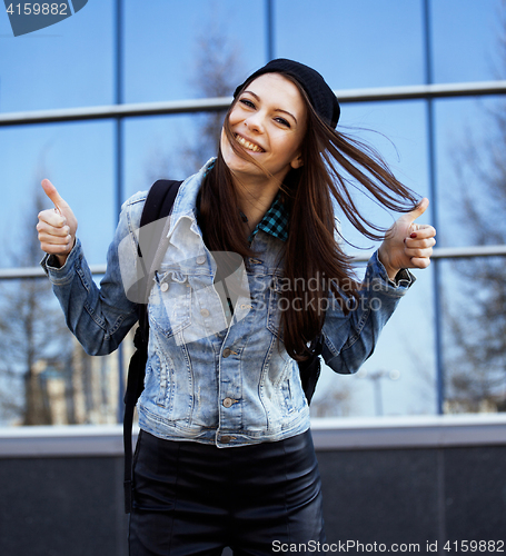 Image of cute brunette teenage girl in hat, student outside at business building