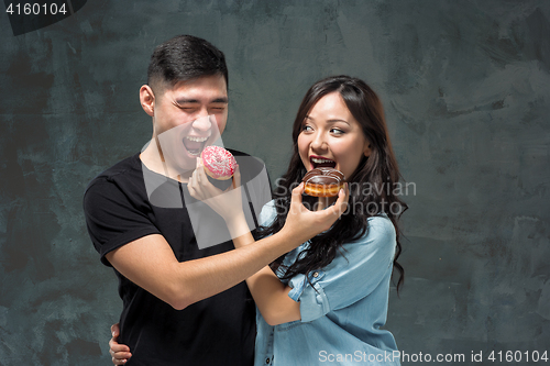 Image of Young asian couple enjoy eating of sweet colorful donut