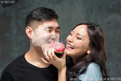 Image of Young asian couple enjoy eating of sweet colorful donut