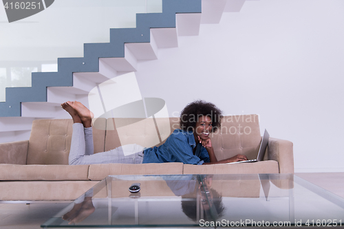 Image of African American woman using laptop on sofa