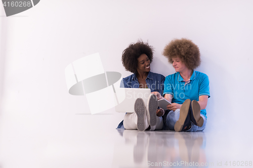 Image of multiethnic couple sitting on the floor with a laptop and tablet