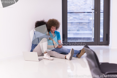 Image of multiethnic couple sitting on the floor with a laptop and tablet