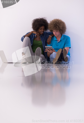 Image of multiethnic couple sitting on the floor with a laptop and tablet