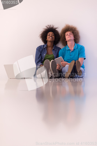 Image of multiethnic couple sitting on the floor with a laptop and tablet