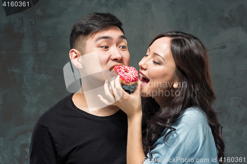 Image of Young asian couple enjoy eating of sweet colorful donut