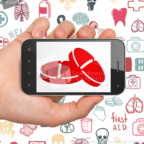 Image of Medicine concept: Hand Holding Smartphone with Pills on display