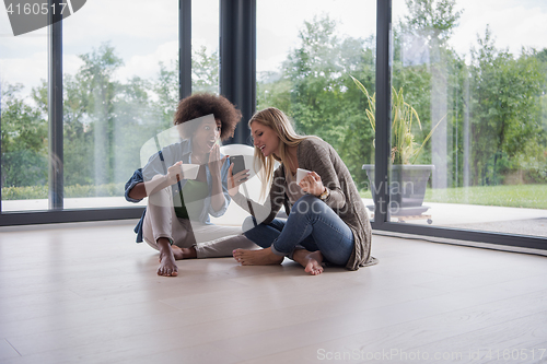 Image of multiethnic women sit on the floor and drinking coffee