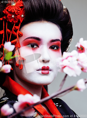 Image of young pretty geisha in black kimono among sakura, asian ethno