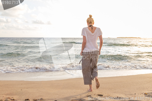 Image of Woman walking on sand beach at golden hour