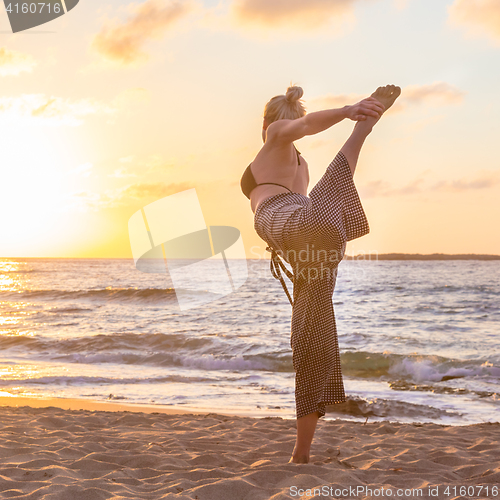 Image of Woman practicing yoga on sea beach at sunset.