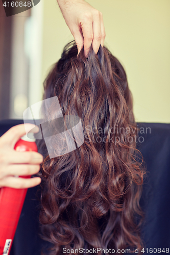 Image of stylist with hair spray making hairdo at salon