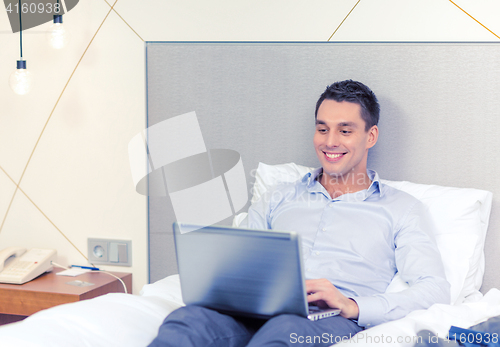 Image of happy businesswoman with laptop in hotel room