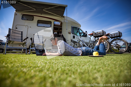 Image of Woman on the grass, looking at the laptop near the campe.