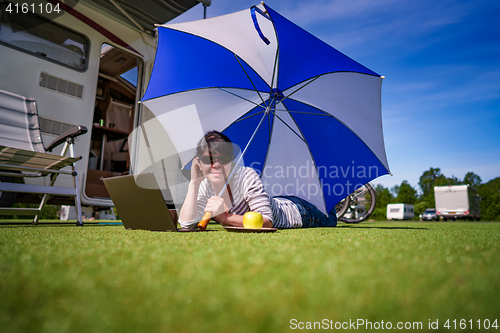 Image of Woman on the grass, looking at the laptop under umbrella near th