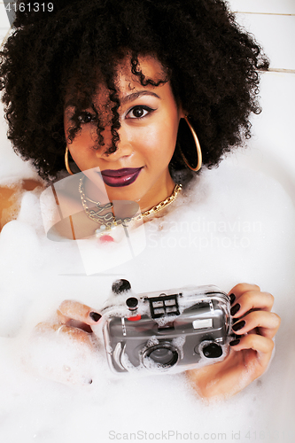 Image of young afro-american teen girl laying in bath with foam, wearing 