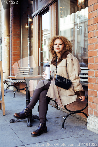 Image of young pretty african american women drinking coffee outside in c