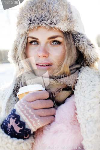 Image of young pretty teenage hipster girl outdoor in winter snow park having fun drinking coffee, warming up happy smiling, lifestyle people concept