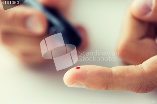 Image of close up of male finger with blood and glucometer