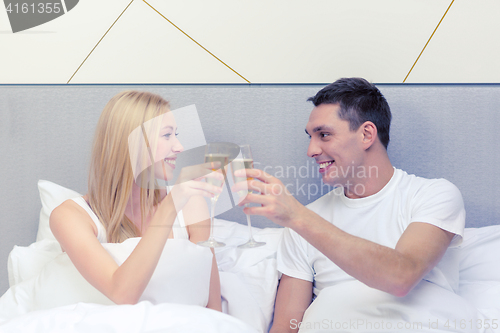 Image of smiling couple with champagne glasses in bed