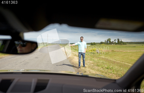 Image of man hitchhiking and stopping car with thumbs up