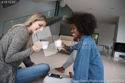 Image of young multiethnic women sit on the floor and drinking coffee