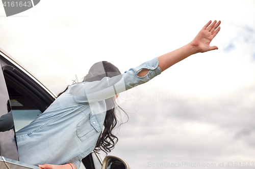 Image of happy woman waving hand leaning out of car window