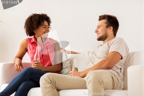 Image of happy friends or couple with beer talking at home