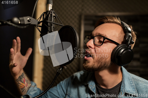 Image of man with headphones singing at recording studio