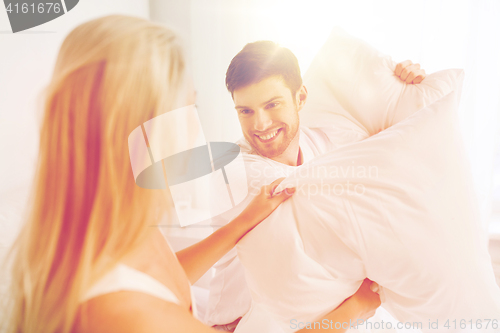 Image of happy couple having pillow fight in bed at home