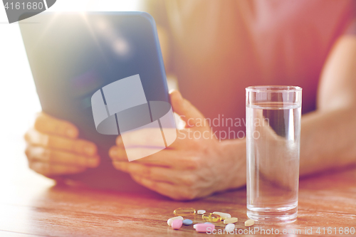 Image of close up of hands with tablet pc, pills and water