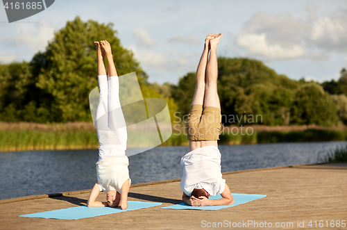 Image of couple making yoga headstand on mat outdoors