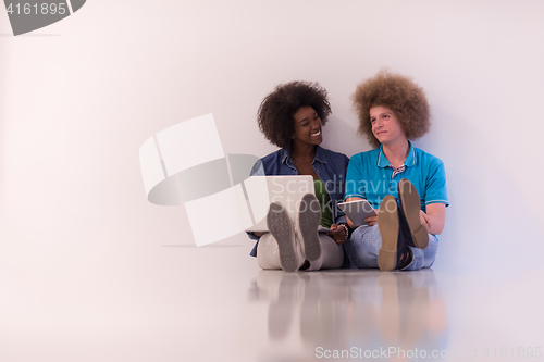 Image of multiethnic couple sitting on the floor with a laptop and tablet