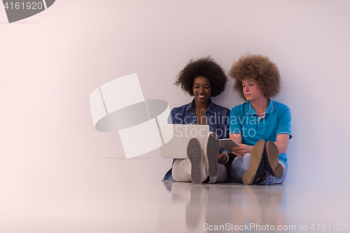 Image of multiethnic couple sitting on the floor with a laptop and tablet