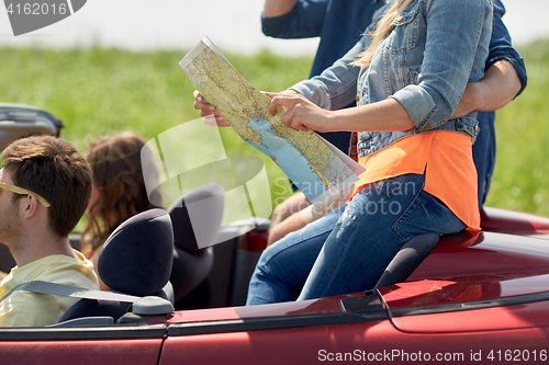 Image of happy friends with map driving in convertible car