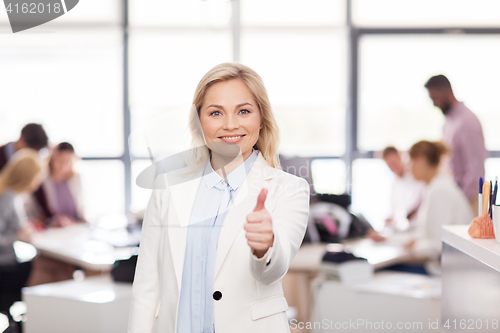 Image of happy businesswoman showing thumbs up at office