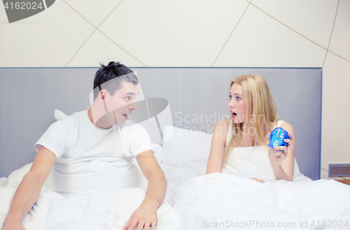 Image of surprised couple with clock in bed