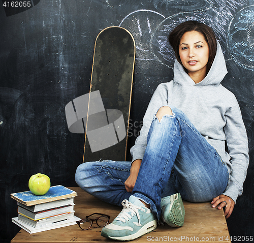 Image of young cute teenage girl in classroom at blackboard seating on ta