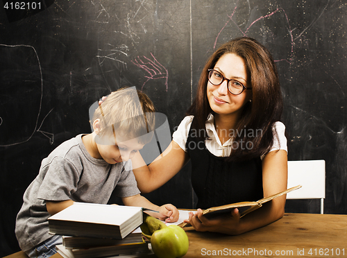 Image of little cute boy with young teacher in classroom studying at blac