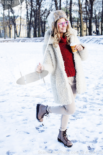Image of young pretty teenage hipster girl outdoor in winter snow park having fun drinking coffee, warming up happy smiling, lifestyle people concept