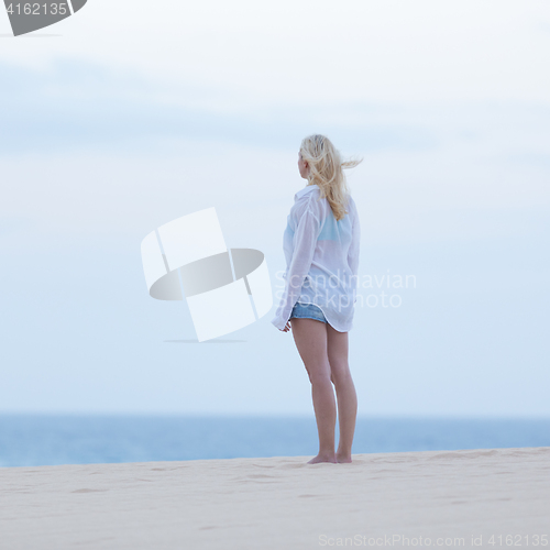 Image of Woman on sandy beach in white shirt at dusk. 