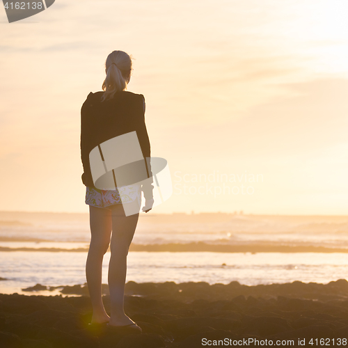 Image of Woman on sandy beach watching sunset.