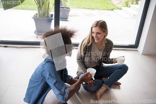 Image of multiethnic women sit on the floor and drinking coffee