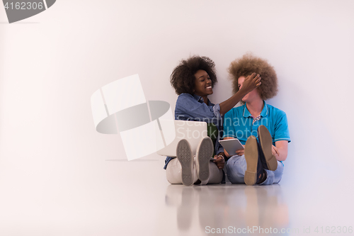 Image of multiethnic couple sitting on the floor with a laptop and tablet