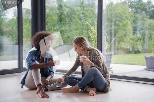 Image of multiethnic women sit on the floor and drinking coffee