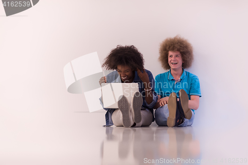 Image of multiethnic couple sitting on the floor with a laptop and tablet